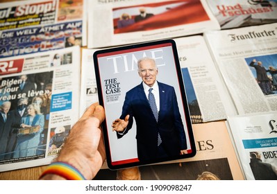 Paris, France - Jan 21, 2021: Man holding digital tablet with Time magazine cover Featuring Joe Biden and stack with International Newspapers headline with Joe Biden and First lady, the newly elected