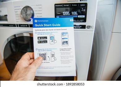 Paris, France - Jan 5, 2020: POV Male Hand Holding Bosch Home Connect Quick Start Guide With Two Latest Siemens Washing And Drying Machine In Background