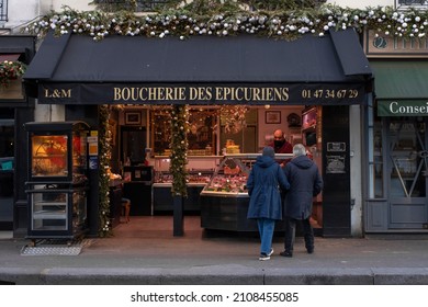 Paris, France - January 14 2022: Old Couple Standing In Front Of Butchery Shop And Choosing Fresh Meat In Paris City Centre On A Cloudy Winter Morning.