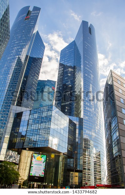 Paris, France - July 10, 2018: Bottom view of the\
glass skyscrapers of the business district of Paris La Defense\
against a blue cloudy\
sky