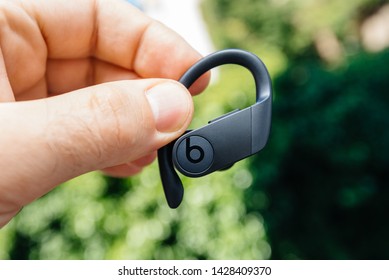 Paris, France - Jun 17, 2019: Close-up of man hand holding new Powerbeats Pro Beats by Dr Dre wireless high-performance earphone with integrated Siri - green park forest background