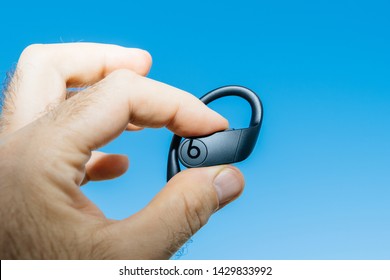 Paris, France - Jun 17, 2019: Close-up of man fingers holding demonstrating new Powerbeats Pro Beats by Dr Dre wireless high-performance earphone with integrated Siri - blue sky square image