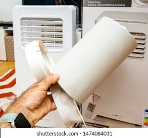 Paris, France - Jun 23, 2019: Young Man Unboxing Installing New Portable Air Conditioner Unit AC During Hot Summer In His Living Room Inspecting The Supplied Accessories