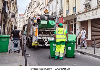 Paris, France - June 18, 2015: Garbage collector in uniform with green plastic containers and garbage truck cleaning the street