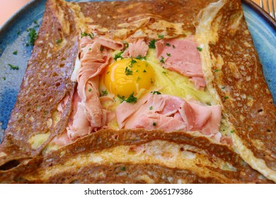 Paris, France, June, 2021: A Classic Ham And Cheese Crêpe Topped With A Runny Egg Sunnyside-up On An Outdoor Patio Of A Parisian Crêperie Café.