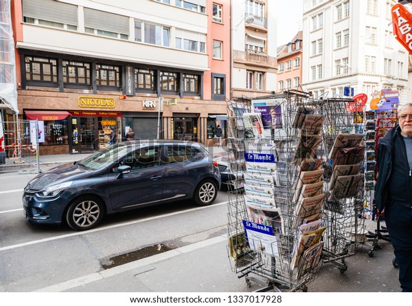 Paris, France - Mar 12, 2019: French press\
kiosk media stand with pedestrians walking and cars parked nearby\
journalism mass media\
distribution