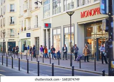 PARIS, FRANCE - MARCH 24, 2020: Long Line Outside Of Monoprix Supermarket With People Standing Far Away From Each Other To Avoid Contagion In Paris During Outbreak Of Coronavirus