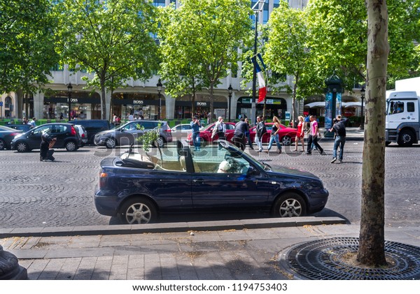 Paris, France - May 07,2011: Photographers shoot a\
fashion event in the middle of the Champ-Elysees in Paris. On the\
side of the street is a small white dog sitting up in the front of\
a open top car.