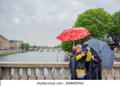 Paris / France - May 14, 2018: Beautiful Older Couple Takes A Selfie In The Rain Over The Seine River, With Colorful Umbrellas. Millions Visit Paris Yearly.