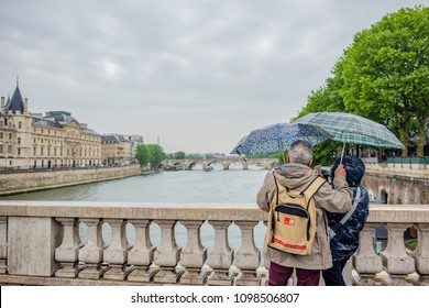 Paris / France - May 14, 2018: Beautiful Older Couple Takes A Selfie In The Rain Over The Seine River, With Colorful Umbrellas. Millions Visit Paris Yearly.