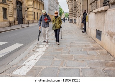 Paris \ France - May 15, 2018: An Older Couple Walks Together Over The Stone Sidewalk On The Famous Street, Rue De Varenne, Site Of Embassies And Other Government Buildings.