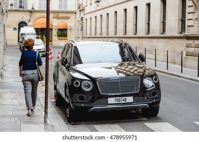 PARIS, FRANCE - MAY 21, 2016: Woman admiring the luxury Bentley Bentayga Hybrid SUV on the streets of Paris, France