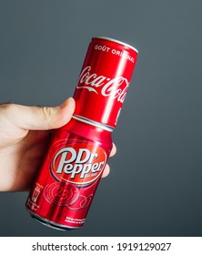 Paris, France - May 3, 2020: POV male hand holding aluminum can of Coca Cola and Dr Pepper manufactured by Dr Pepper Snapple Group soft sweet drinks - isolated against gray background