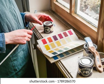 Paris, France - May 30, 2020: Side View Of Woman Looking At The Colour Chart With Sample Pot Of Farrow And Ball Luxury British Paint Preparing To Paint The Wall And Window Frame