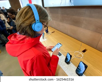 Paris, France - Nov 02, 2019: Side view woman in red coat inside Apple Computers Store testing listening to music with new latest Beats by Dr Dre Solo Pro Active Noise Cancelling headphones