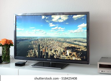 PARIS, FRANCE - NOV 21, 2015: Apple TV 4k Device Next To 4k Pansonic Plasma OLED Display Projecting The Typical Apple Screensaver Of Aerial City