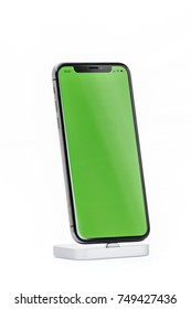 PARIS, FRANCE - NOV 5, 2017: New Apple iPhone X 10 smartphone in docking station charging with green chroma key backdrop against white background in male hand