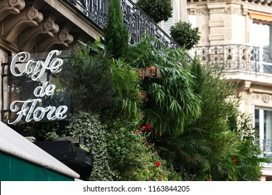 Paris, France - November 01, 2017: The Famous Cafe De Flore. Saint-Germain Boulevard. Signboard Of The Cafe Decorated With Green Plants. Autumn Paris. Typical Parisian Houses With Balconies. 