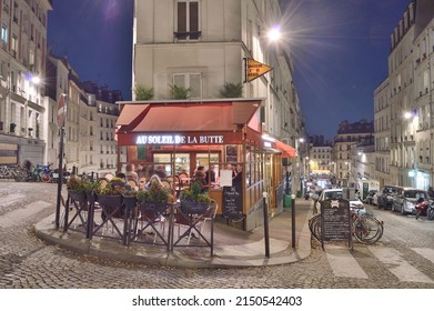 Paris, France - November 12, 2021: Old streets of Montmartre at night in Paris, France. Parisians and tourists enjoy food and drinks at the street french cafe.