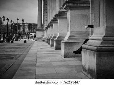 Paris, France - November 23, 2017: Black and white perspective from Louvre museum building with woman taking a rest on the stone benches.