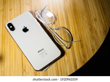 Paris, France- Oct 2, 2018: Latest Apple Computers Smartphone mobile telephone iPhone XS 11 12 13 Pro Max on wooden luxury table with titanium eyewear spectacles near - tilt-shift focus on iPhone word