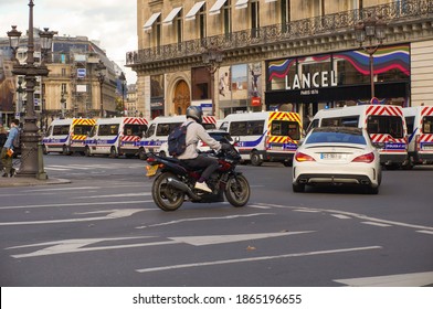 Paris, France - Oct. 2020 - A Motorbike And A Mercedes Car Pass By A Convoy Of The Crowd Control Units Of The French National Police, In Place De L'Opéra Square, In Front Of A Lancel Luxury Store