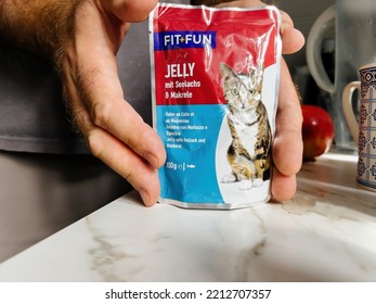 Paris, France - Sep 13, 2022: POV Male Hand Holding Pouch With Fit Plus Fun Wet Cat Food Jelly With Salmon And Fish Taste - Modern Kitchen Background Preparing To Feed The Pet Cat Animal