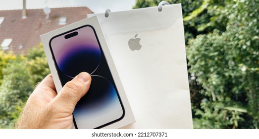 Paris France - Sep 18 2022: POV Male Hand Holding New Apple Computers Iphone 14 Pro Cardboard Box With Present Paper Bag With Iconic Logotype - Garden Green Background