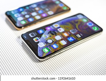 PARIS, FRANCE - SEP 27, 2018: Tilt-shift focus lens over two new Apple Computers iPhone Xs and Xs Max with home apps on the gorgeous OLED display on stripe cardboard background - side view