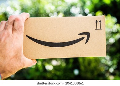 Paris, France - Sep 8, 2021: POV Personal Perspective Male Hand Holding Amazon Prime Cardboard Package Carton Box WithSmile Logotype Arrow - Recycling Material After Unboxing