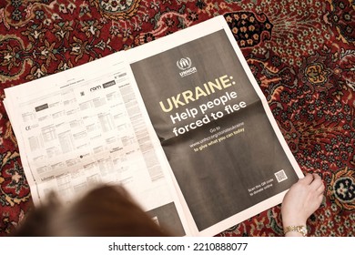 Paris, France - Sep 9, 2022: Woman Reading On Living Room Floor Carpet Latest Financial Times Newspaper With UNCHR Advertising On One Large Page Ukraine Help People Forced To Flee