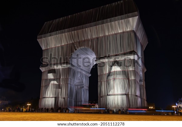 Paris, France-September 2021; Low angle view by\
night of wrapped and illuminated Arc de Triomphe art installation\
by Christo on Place Charles de Gaulle; blue, white and red light\
streaks of cars