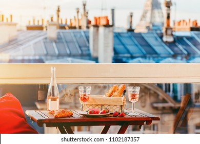 Paris luxury lifestyle. Pink wine in two glasses, traditional french bakery products - baguettes, macaron, croissant and strawberries on a balcony with a view on rooftops and Eiffel Tower - Powered by Shutterstock