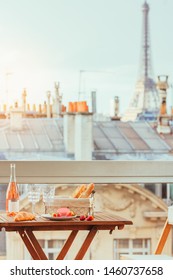 Paris luxury lifestyle. Pink wine, two glasses, traditional french bakery products - baguettes, macaron, croissant and strawberries on a balcony with a view on rooftops and Eiffel Tower.