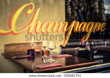 Paris Restaurant With Champagne Sign In The Window With Place Settings And Wine Glasses