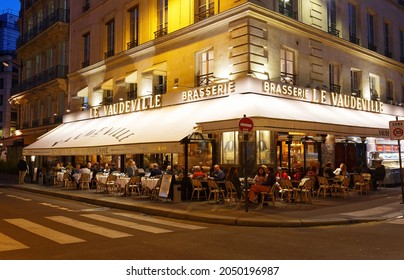 Paris,France-September 27, 2021 : The traditional French brasserie Le Vaudeville at night. It is located near Brogniart palace in Paris. Inscription in French on sign: 100 years of parisian life.