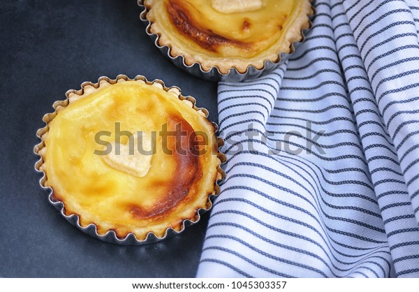 
Parisian Flan (French Custard Pie) Classic tart. Baked
confectionery cream in shortbread dough crust. Two mini pies on
dark background with leaves and light stripes textile.
