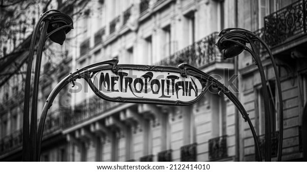 Parisian metropolitan (metro, subway) sign in a street\
during the day. Typical house in the background. Old times,\
vintage, nostalgia concept. Historic black and white photo. Paris,\
France. 
