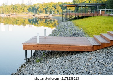 Park Area For Walks Within The City, A Wooden Pier For Mooring Boats, Early In The Morning, A Bank Of Rubble, A City Recreation Park, No People. High Quality Photo