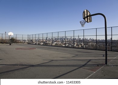 A Park Basketball Court In Jersey City, With The New York Skyline Visible Behind.