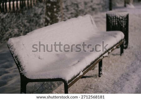 Park bench covered in a thick layer of fresh, undisturbed white snow during a quiet winter night, conveying feelings of solitude, cold weather, and peaceful stillness in a public park setting