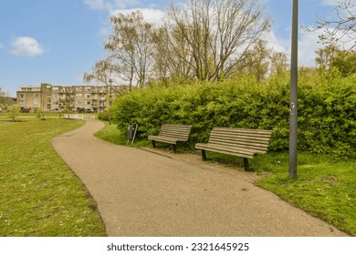 a park bench in the middle of an urban area with trees and bushes on either side of the path that leads to apartment buildings - Powered by Shutterstock