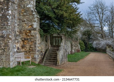 Park Bench Next To Some Stone Steps With A Stone Bannister And Blossom On Trees In The Background