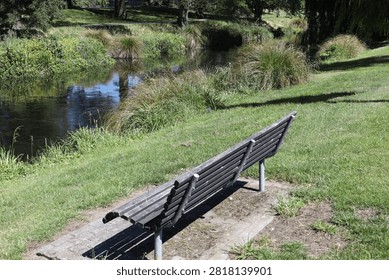 park bench, simple functional design, dark wooden slats, sturdy metal legs, scenic view nearby creek, lush greenery (wide-angle, landscape, bright-sunshine)