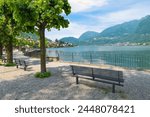 Park with benches on the shore of a lake surrounded by mountains. Lake Lugano and the town of Riva San Vitale, Switzerland, at the foot of Monte San Giorgio UNESCO site for fossiliferous deposits