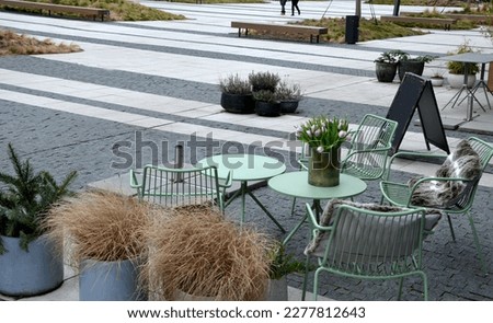 Park furniture chess table and chairs, stripes, tiles four persons made of light metal and wooden beams with backrest
on bright glade area gravel lawn green beige gray evening sun spring