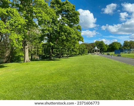 Park landscape, with sloping banks, old trees, and a distant Victorian bandstand, on a summers day in, Lister Park, Bradford, UK