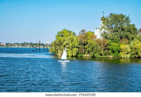 Park Monastery Island, Dnepropetrovsk.\
Restaurant, cable car, floating kayaks and sailing boat, green\
trees, River Dnepr. Blue water, sky, early\
autumn
