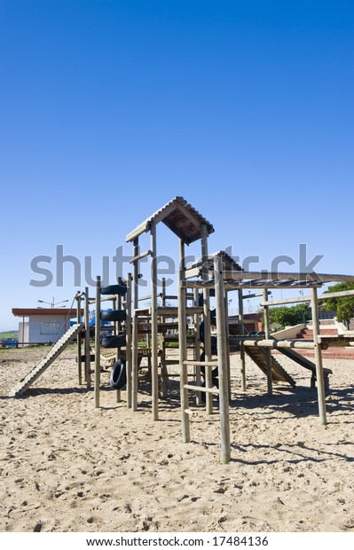 A park next to the beach with a play\
area for kids containing a wooden\
jungle-jim.