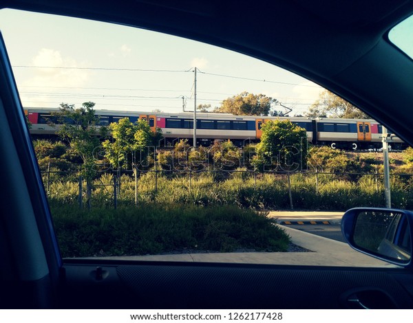 Park and ride rail concept. An Australian\
train is seen travelling past a parked vehicle. Passengers often\
park in car parks to catch the commuter\
rail.